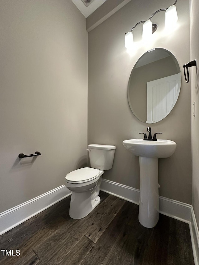 half bathroom with visible vents, baseboards, toilet, wood finished floors, and a sink