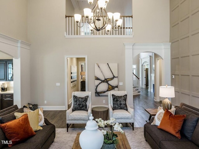 living area featuring arched walkways, a towering ceiling, wood finished floors, stairs, and a chandelier