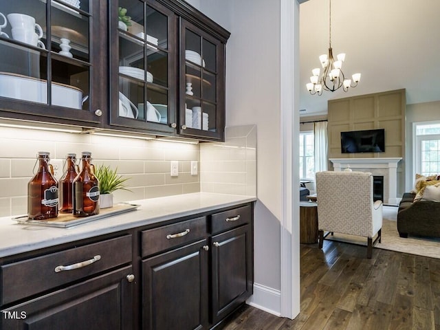 bar with baseboards, hanging light fixtures, decorative backsplash, dark wood-style floors, and a glass covered fireplace