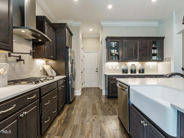 kitchen featuring dark wood-type flooring, light countertops, appliances with stainless steel finishes, wall chimney exhaust hood, and glass insert cabinets