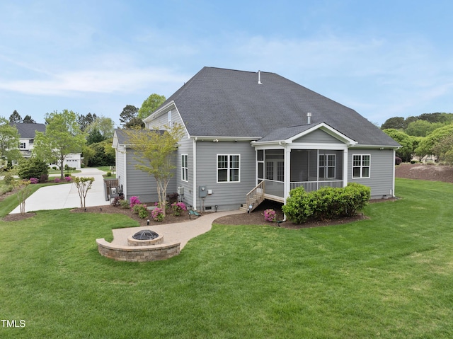 rear view of house featuring a shingled roof, a lawn, an outdoor fire pit, and a sunroom