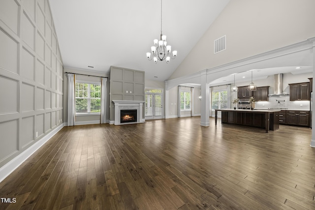unfurnished living room with high vaulted ceiling, a chandelier, a wealth of natural light, dark wood-style flooring, and visible vents