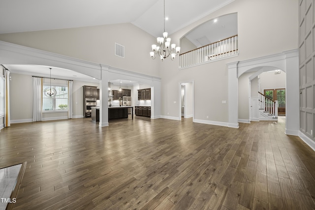 unfurnished living room featuring high vaulted ceiling, a notable chandelier, stairs, dark wood-style flooring, and visible vents