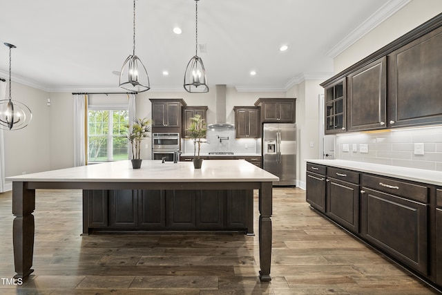 kitchen with recessed lighting, stainless steel appliances, light countertops, wall chimney exhaust hood, and a breakfast bar area