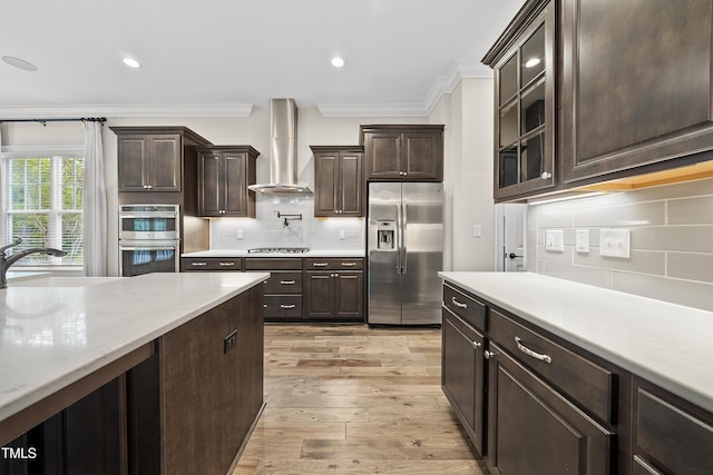 kitchen featuring wall chimney range hood, crown molding, dark brown cabinets, a sink, and appliances with stainless steel finishes