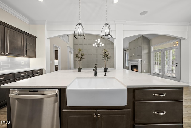 kitchen with a sink, tasteful backsplash, dark brown cabinetry, dishwasher, and a lit fireplace