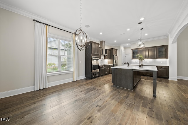 kitchen featuring stainless steel appliances, dark brown cabinets, wall chimney range hood, crown molding, and light countertops