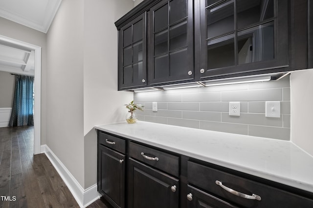 bar with dark wood-style flooring, ornamental molding, tasteful backsplash, and baseboards