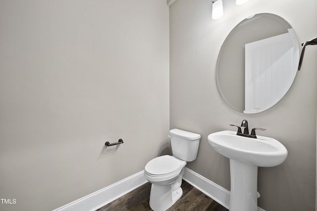 half bathroom with baseboards, toilet, wood finished floors, and a sink