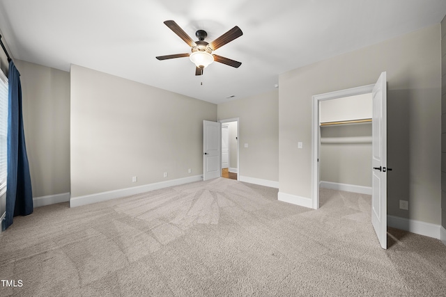 unfurnished bedroom featuring carpet floors, a spacious closet, baseboards, and ceiling fan