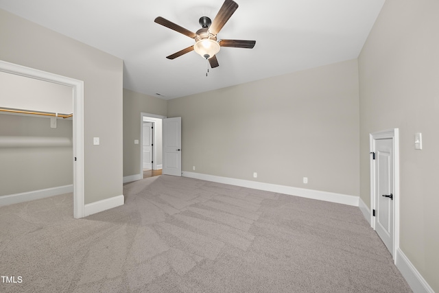 unfurnished bedroom featuring a walk in closet, carpet, a ceiling fan, and baseboards