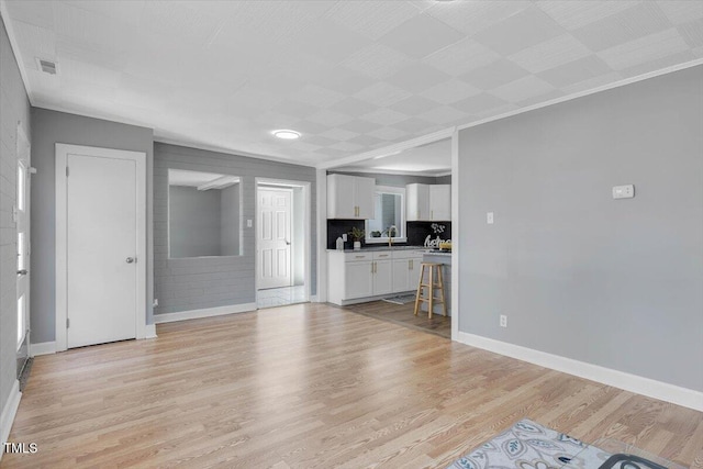 unfurnished living room with ornamental molding, sink, and light hardwood / wood-style floors