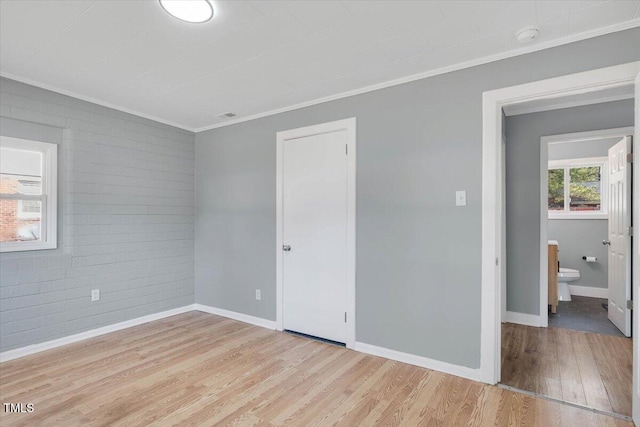 unfurnished bedroom with crown molding, brick wall, connected bathroom, and light wood-type flooring