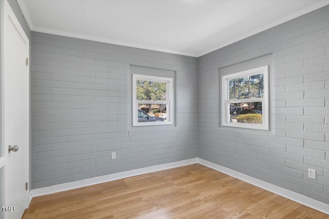 unfurnished room featuring crown molding, brick wall, light wood-type flooring, and a wealth of natural light