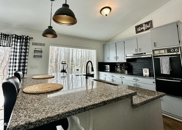 kitchen featuring sink, vaulted ceiling, hanging light fixtures, dark stone countertops, and double wall oven