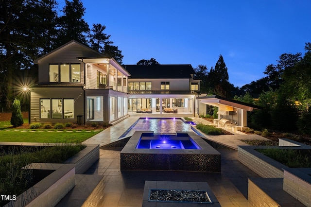 back house at dusk with a multi sided fireplace, a balcony, a patio, a yard, and a pool with hot tub