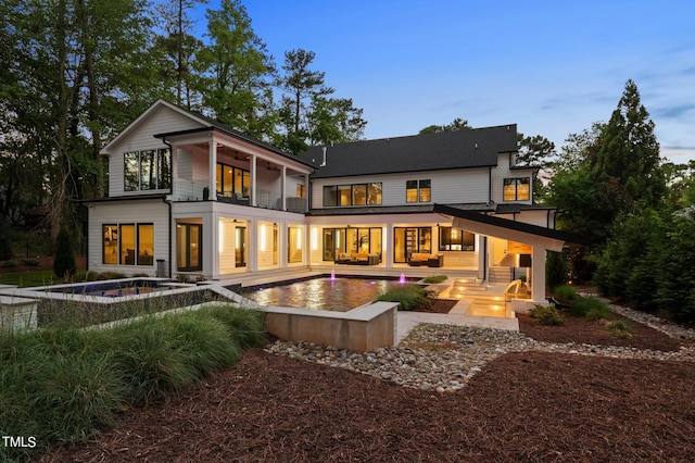 back house at dusk with a balcony, a swimming pool with hot tub, and a patio