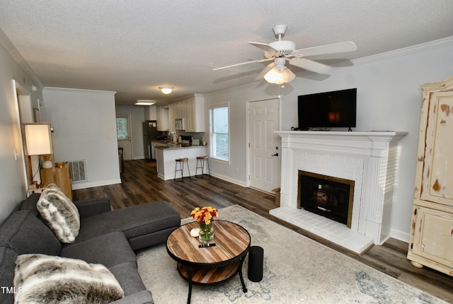 living room with crown molding, dark hardwood / wood-style flooring, a brick fireplace, and a textured ceiling