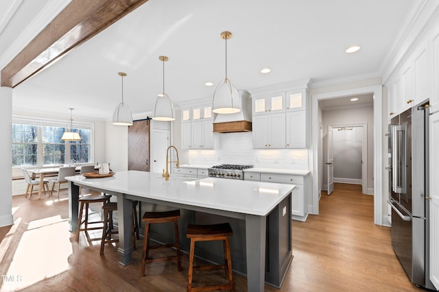 kitchen featuring high end fridge, light countertops, custom range hood, decorative backsplash, and a sink