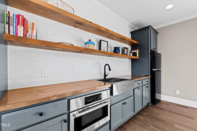 kitchen featuring open shelves, wooden counters, ornamental molding, stainless steel oven, and a sink