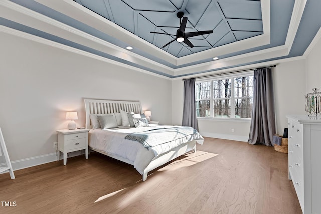 bedroom featuring ornamental molding, a tray ceiling, baseboards, and wood finished floors