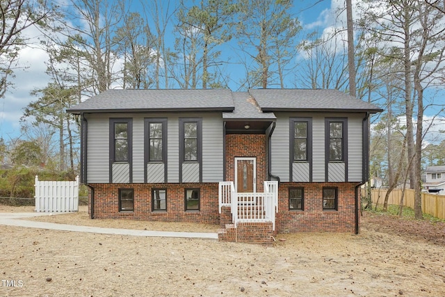 view of front of house with brick siding, roof with shingles, and fence