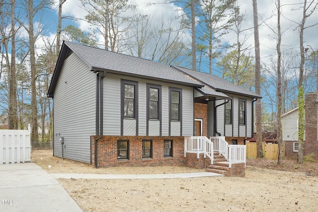 bi-level home featuring fence, brick siding, and roof with shingles