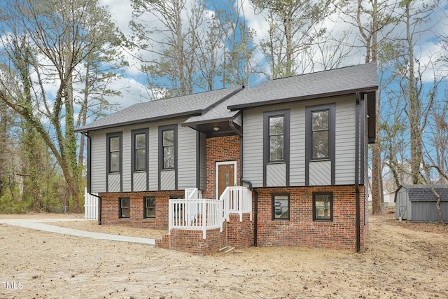 split foyer home with brick siding, roof with shingles, an outdoor structure, and a shed