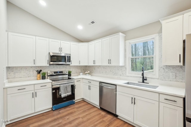 kitchen featuring visible vents, a sink, stainless steel appliances, vaulted ceiling, and white cabinetry