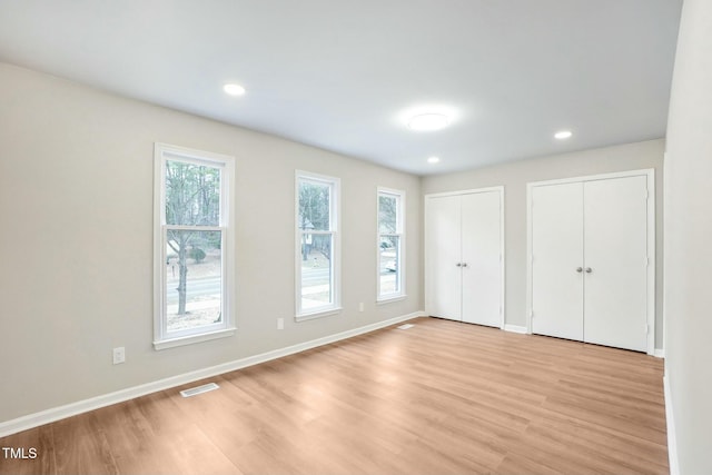 unfurnished bedroom with visible vents, baseboards, recessed lighting, light wood-type flooring, and two closets