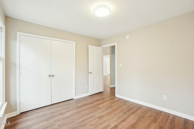 unfurnished bedroom featuring a closet, light wood-style flooring, and baseboards