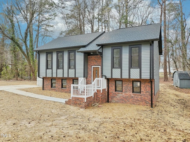 split foyer home featuring a storage unit, brick siding, an outdoor structure, and a shingled roof