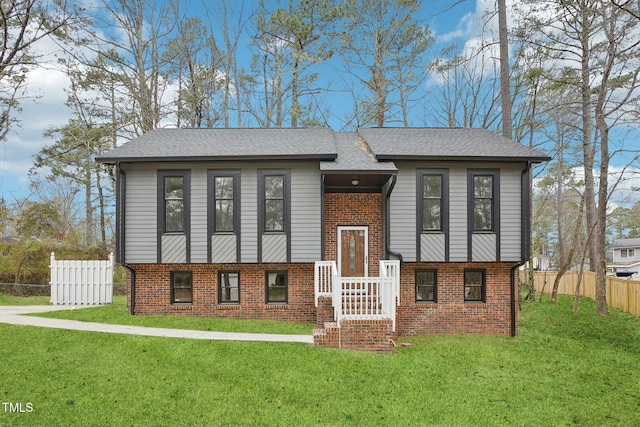 view of front of home with a front lawn, fence, brick siding, and a shingled roof