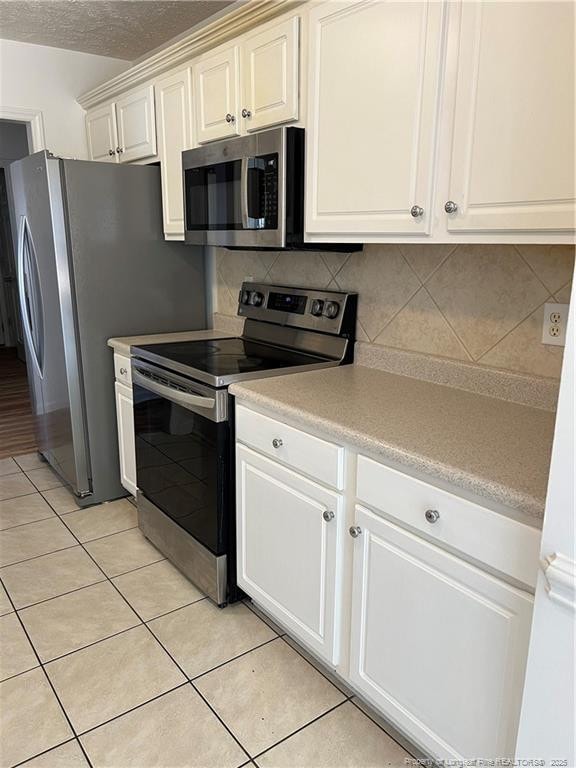 kitchen with white cabinets, stainless steel appliances, light countertops, backsplash, and light tile patterned flooring