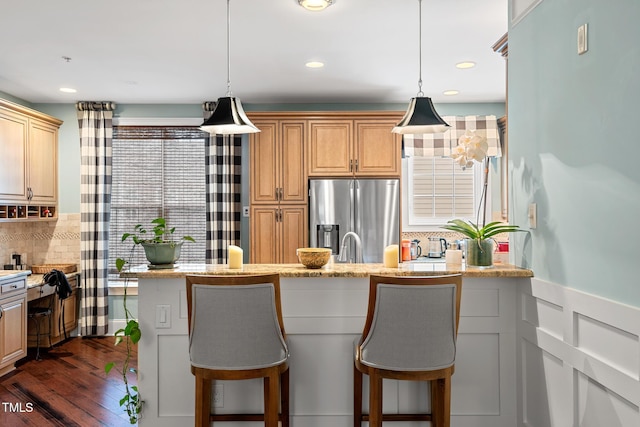 kitchen with pendant lighting, stainless steel fridge, light stone countertops, and a breakfast bar area