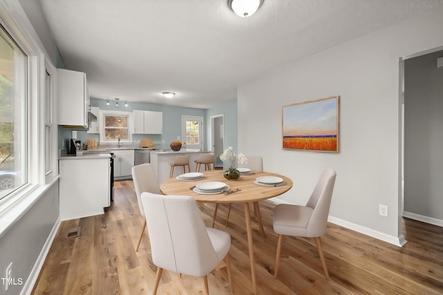 dining area with rail lighting, sink, and light hardwood / wood-style flooring