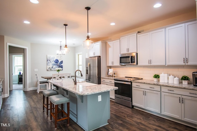 kitchen featuring an island with sink, appliances with stainless steel finishes, dark wood finished floors, and backsplash