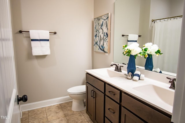 full bath featuring double vanity, a sink, toilet, and baseboards