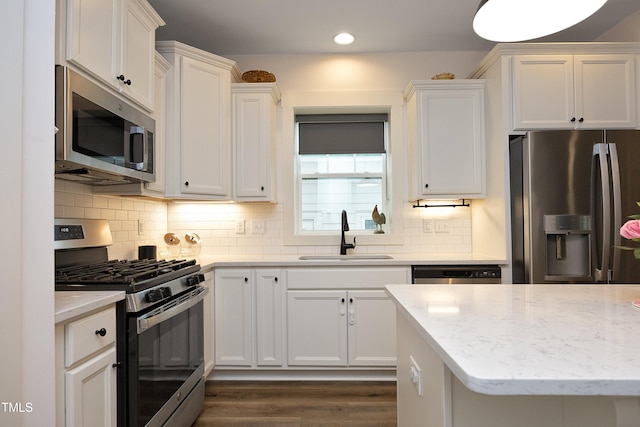 kitchen featuring appliances with stainless steel finishes, sink, white cabinets, decorative backsplash, and light stone counters