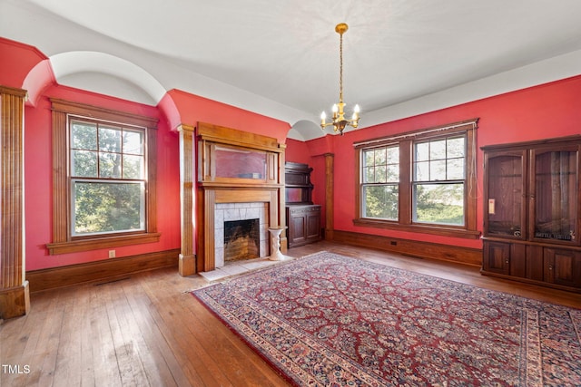 unfurnished living room featuring a tiled fireplace, plenty of natural light, a notable chandelier, and light hardwood / wood-style flooring