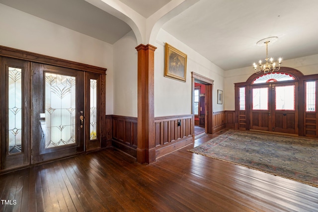 entrance foyer with ornate columns, dark wood-type flooring, and an inviting chandelier