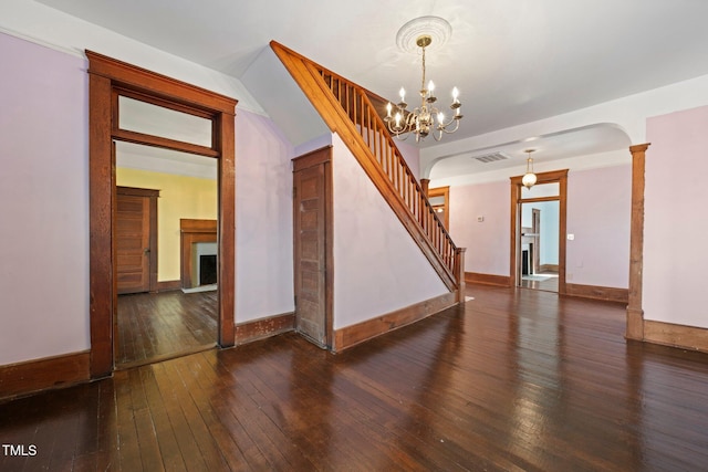 empty room with ornate columns, an inviting chandelier, and dark hardwood / wood-style flooring