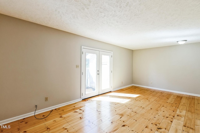 empty room with light wood finished floors, french doors, a textured ceiling, and baseboards