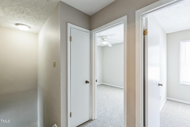 hall featuring carpet flooring, baseboards, and a textured ceiling