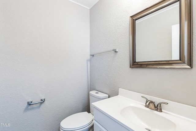 bathroom with vanity, toilet, and a textured wall