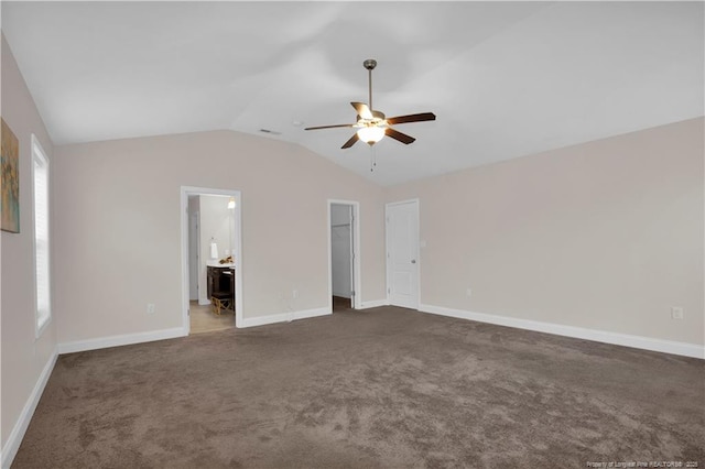 interior space with connected bathroom, dark carpet, vaulted ceiling, and a spacious closet