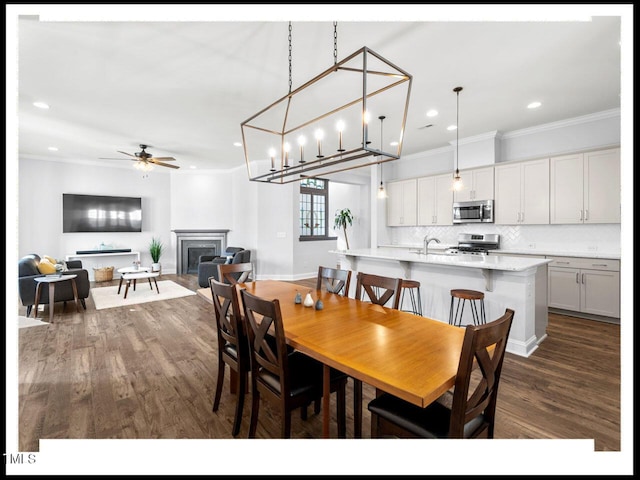 dining space with ornamental molding, a ceiling fan, dark wood finished floors, recessed lighting, and a fireplace