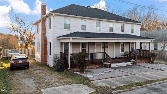 view of front facade with a shingled roof, covered porch, driveway, and a chimney