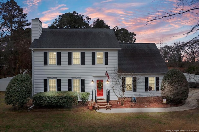 colonial house featuring a chimney, a yard, and a shingled roof