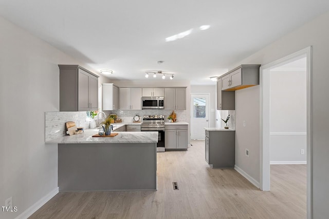 kitchen featuring stainless steel appliances, gray cabinets, backsplash, and kitchen peninsula